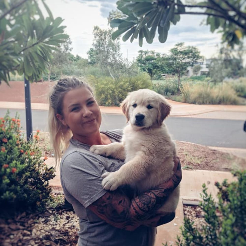 Smiling woman holding a fluffy golden retriever puppy outside