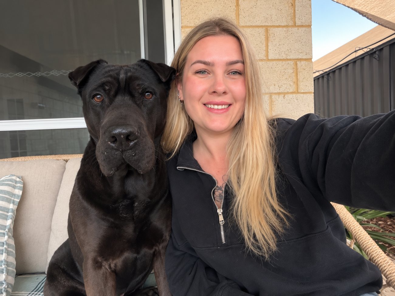 Tyler smiling on an outdoor couch beside her black dog, Jedi